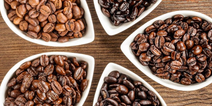 Bowls of coffee beans on wooden table showing different roast levels: light roast, medium roast and dark roast