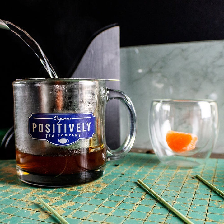 Positively Tea Company Blood Orange Vanilla Rooibos tea being steeped in a branded glass mug, showcasing a rich, aromatic brew.
