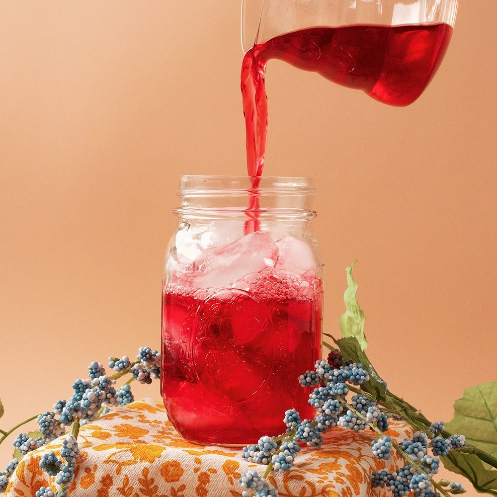 Positively Tea Company Organic Hibiscus tea being poured over ice in a glass jar, creating a vibrant red herbal infusion.
