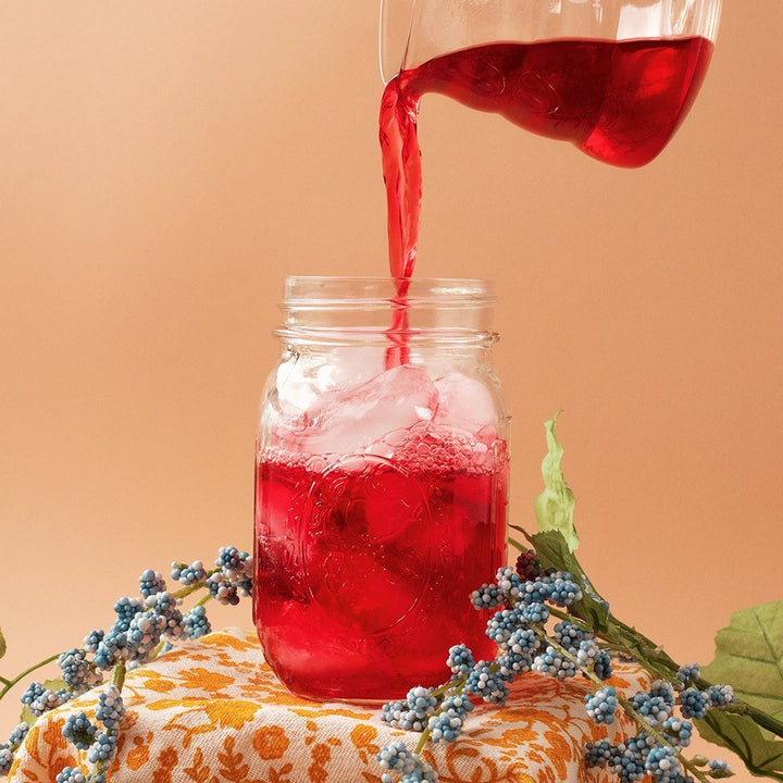 Positively Tea Company Organic Hibiscus tea being poured over ice in a glass jar, creating a vibrant red herbal infusion.