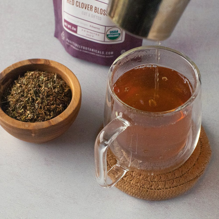 Positively Botanicals Organic Red Clover Blossom herbal supplement steeped in water, creating a soothing nutrient-rich drink.